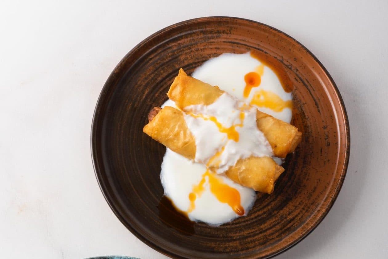 Yeşil Mercimekli Dana Kıymalı Börek on a brown ceramic plate with yoghurt sauce and chilli oil