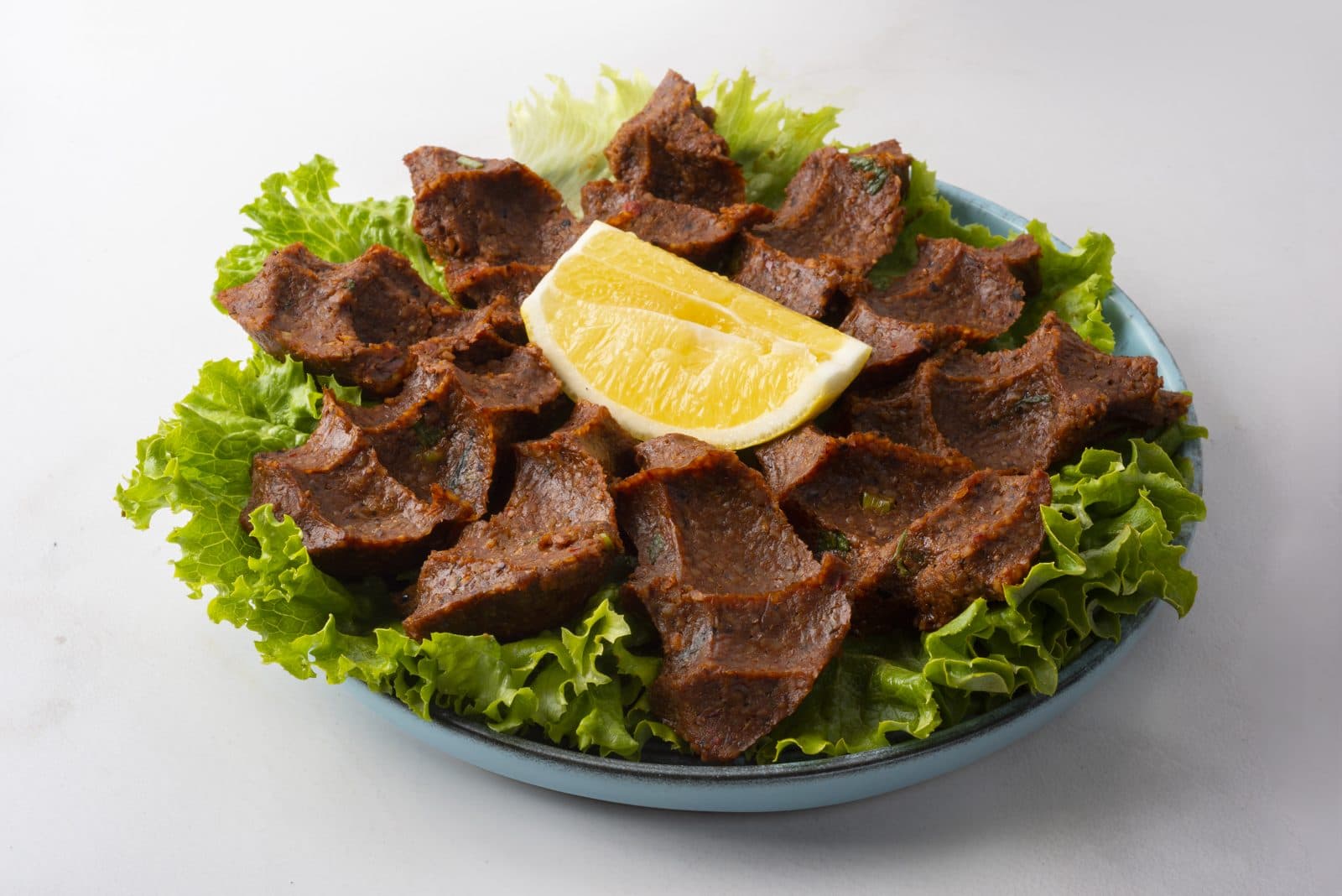 Marul yaprakları üzerinde servis edilmiş etsiz çiğ köfte ve limon dilimi